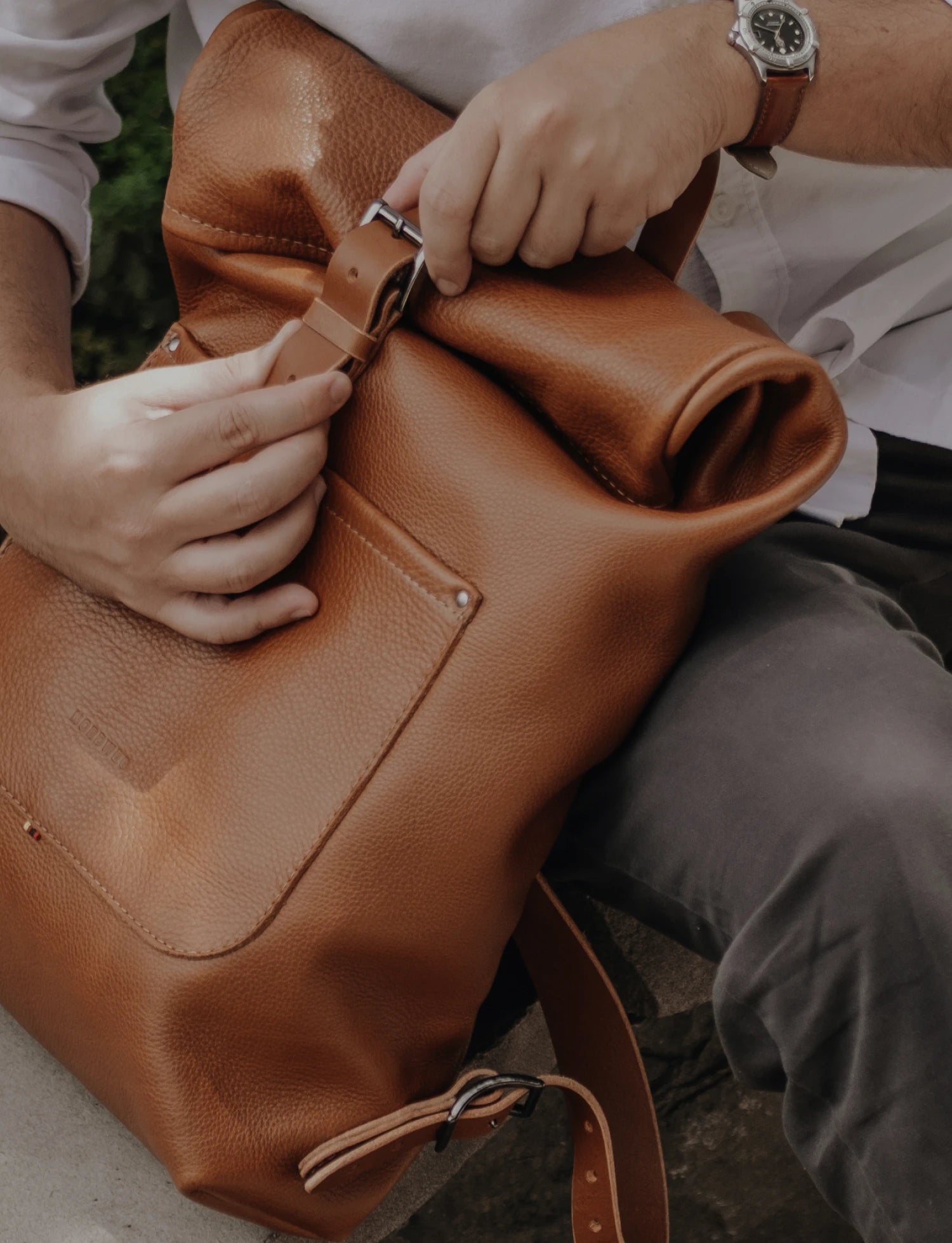 Mãos ajustam a fivela de fechamento da Mochila Legacy Nordweg na cor Cognac