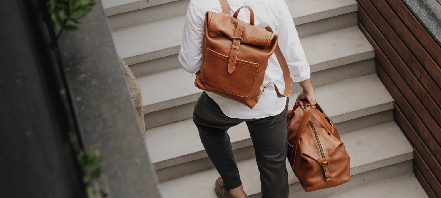 Homem sobe escadaria carregando a Mala Legacy e usando a Mochila Legacy Nordweg na cor Cognac