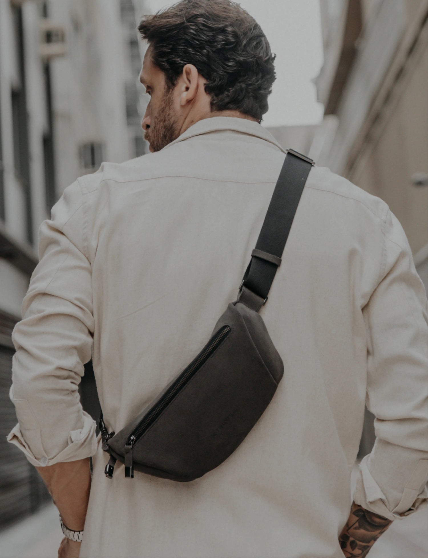 Homem de costas usa a Sling Bag Pulse Limited Edition Nordweg em couro camurça cinza, com alça transversal ajustável